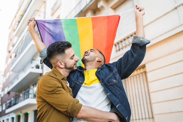 Gay pareja abrazando y mostrando su amor con arco iris bandera. —  Fotos de Stock