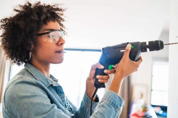 Afro-Frau bohrt Wand mit Elektrobohrmaschine. — Stockfoto