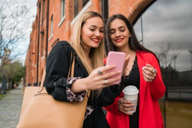 Dışarıda cep telefonlarını kullanan iki genç arkadaş..