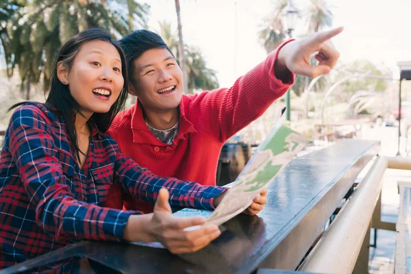 Asiatisches Reisepaar hält eine Landkarte in der Hand und sucht nach einer Wegbeschreibung. — Stockfoto