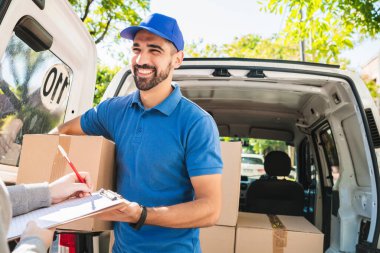 Delivery man carrying package while customer sign in clipboard. clipart