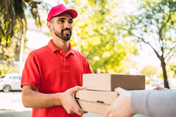 Entrega hombre llevando paquetes mientras que hace entrega a domicilio. —  Fotos de Stock