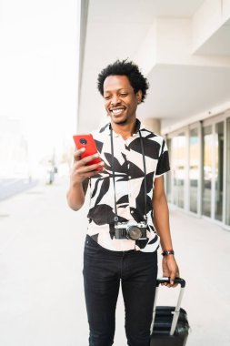 Turist adam cep telefonunu kullanıyor ve dışarıda bavulunu taşıyor..