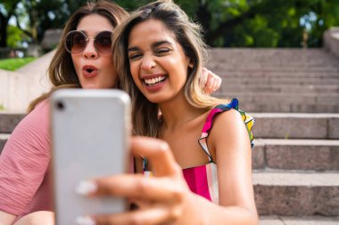 İki arkadaş dışarıda telefonla selfie çekiyor..