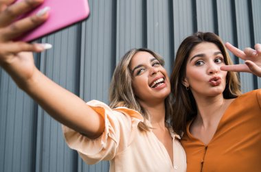 İki arkadaş dışarıda telefonla selfie çekiyor..