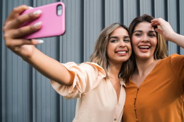 İki arkadaş dışarıda telefonla selfie çekiyor..
