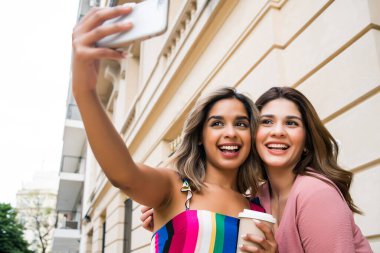 İki arkadaş dışarıda telefonla selfie çekiyor..