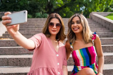 İki arkadaş dışarıda telefonla selfie çekiyor..