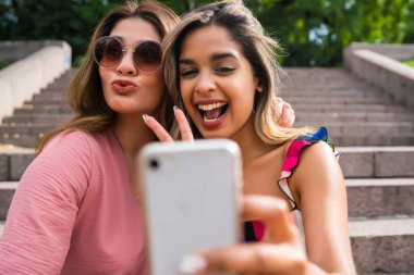 İki arkadaş dışarıda telefonla selfie çekiyor..