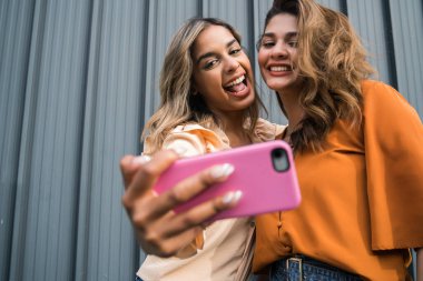 İki arkadaş dışarıda telefonla selfie çekiyor..