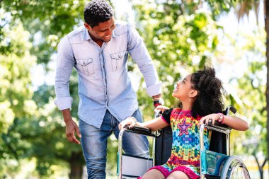 Little girl in a wheelchair at the park with her father.