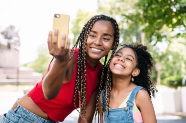 Mother and daughter taking a selfie with a mobile phone outdoors.