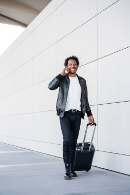 Turist telefonda konuşuyor ve dışarıda bavul taşıyor..