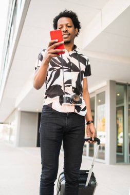 Turist adam cep telefonunu kullanıyor ve dışarıda bavulunu taşıyor..