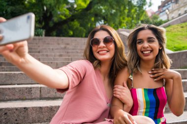 İki arkadaş dışarıda telefonla selfie çekiyor..