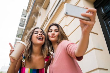 İki arkadaş dışarıda telefonla selfie çekiyor..