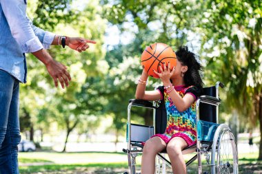 Tekerlekli sandalyede babasıyla basketbol oynayan küçük bir kız..