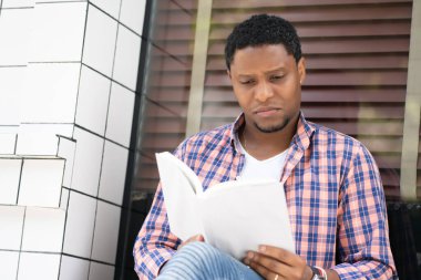 Mağaza vitrininde oturmuş kitap okuyan bir adam..