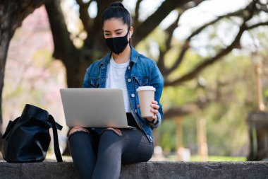 Dışarıda dizüstü bilgisayarını kullanan genç bir kadın..