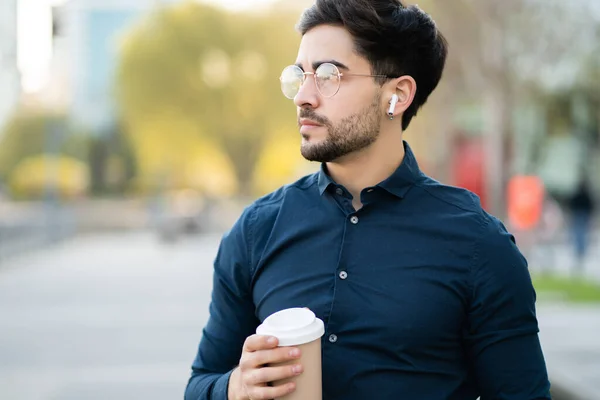 Young man holding a cup of coffee while walking outdoors. — Stock Photo, Image