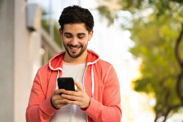 Mladý muž používá svůj mobilní telefon venku. — Stock fotografie