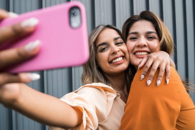 İki arkadaş dışarıda telefonla selfie çekiyor..