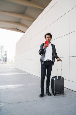Turist adam cep telefonunu kullanıyor ve dışarıda bavulunu taşıyor..