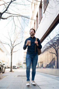 Genç adam dışarıda yürürken elinde bir fincan kahve tutuyor..