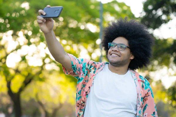 Latin man taking a selfie with phone outdoors.