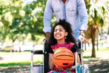 Tekerlekli sandalyede babasıyla basketbol oynayan küçük bir kız..