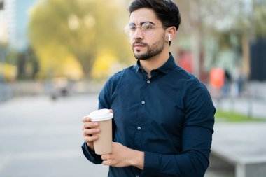 Genç adam dışarıda yürürken elinde bir fincan kahve tutuyor..