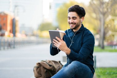 Genç adam dışarıda dijital tabletle video görüşmesi yapıyor..