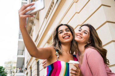 İki arkadaş dışarıda telefonla selfie çekiyor..