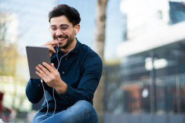 Genç adam dışarıda dijital tabletle video görüşmesi yapıyor..