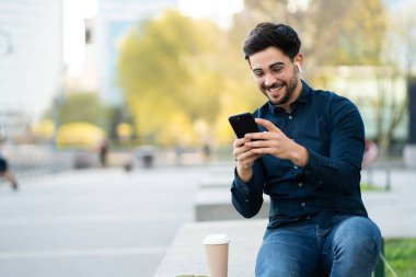 Genç adam cep telefonunu açık havada kullanıyor..