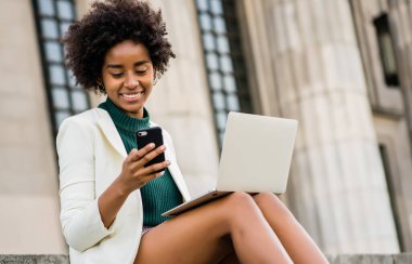 İş kadını cep telefonunu ve bilgisayarını açık havada kullanıyor..