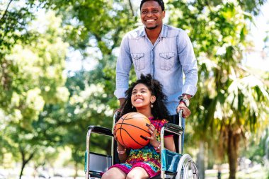Tekerlekli sandalyede babasıyla basketbol oynayan küçük bir kız..