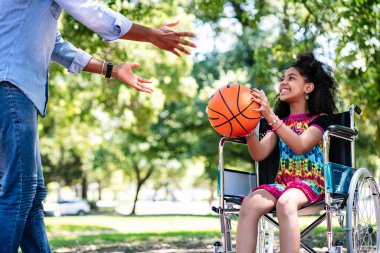 Tekerlekli sandalyede babasıyla basketbol oynayan küçük bir kız..