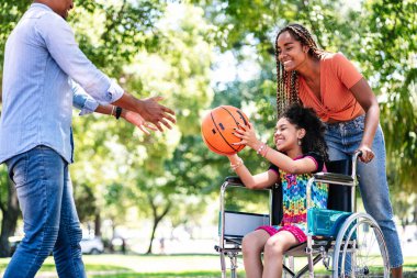 Tekerlekli sandalyede ailesiyle basketbol oynayan bir kız..