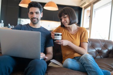 Çift evdeki koltukta otururken dizüstü bilgisayar kullanıyor..