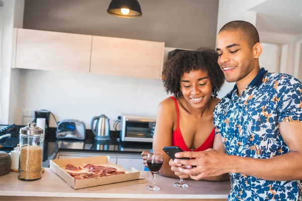 Happy latin couple using mobile phone while having dinner. — Stock Photo, Image