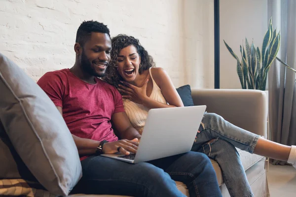 Couple using a laptop while sitting on a couch at home. — Stock Photo, Image