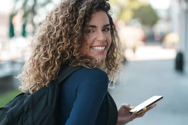 Mujer latina sonriendo mientras usa un teléfono móvil al aire libre en la calle. —  Fotos de Stock