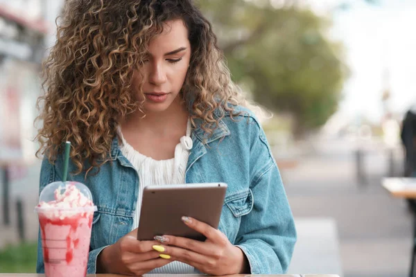 Mujer latina usando una tableta digital mientras está sentada en una cafetería al aire libre. —  Fotos de Stock
