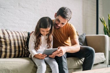 Küçük kız ve babası evde dijital tablet kullanıyorlar..