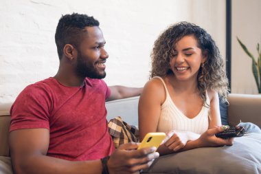 Çift evdeki koltukta otururken cep telefonu kullanıyor..