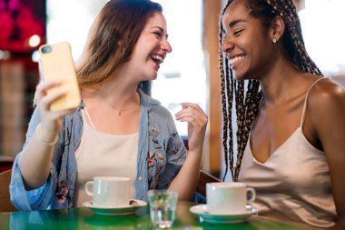 Kahve dükkanında otururken cep telefonu kullanan iki bayan arkadaş..