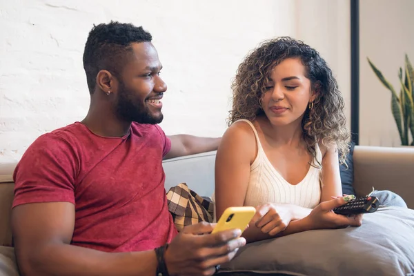 Pareja usando un teléfono móvil mientras está sentado en un sofá en casa. — Foto de Stock