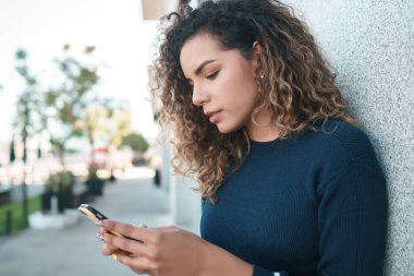 Latin bir kadın sokakta cep telefonunu kullanıyor..