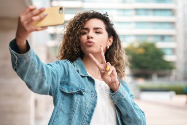 Dışarıda cep telefonuyla selfie çeken genç bir kadın..